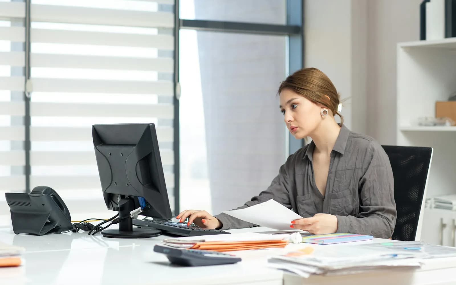 Medewerker op kantoor aan een bureau vol papieren, met een telefoon en een rekenmachine