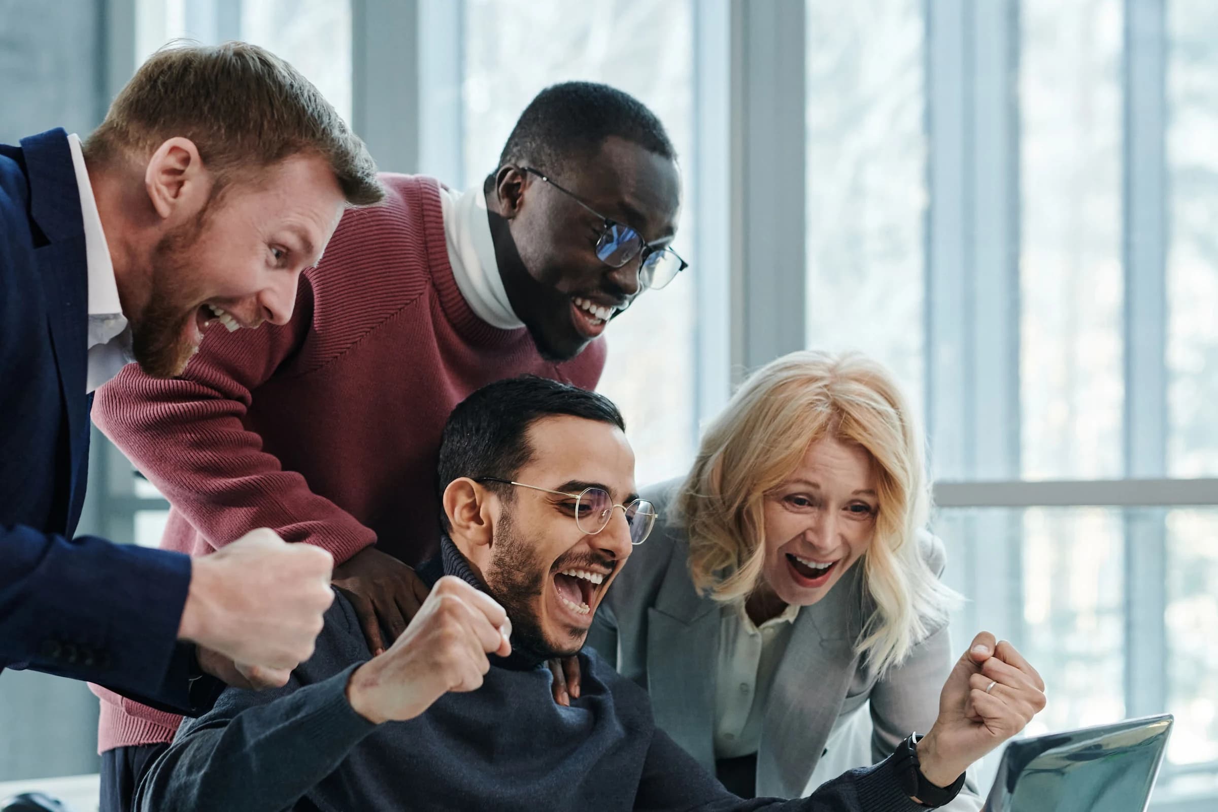 Vier collega's juichen samen bij een laptop op kantoor.